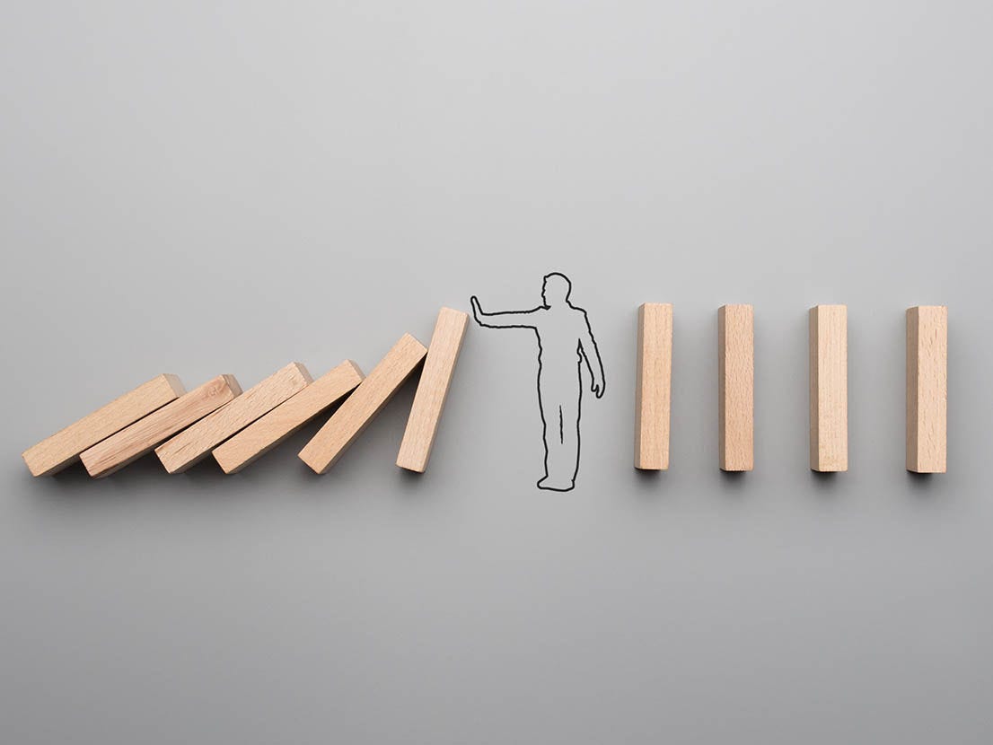Wide cropped image of the outline of a businessman stopping the domino effect on gray background.